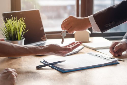 Landlord handing over keys to tenant in an office setting.