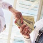 Person handing over a stack of US dollar bills in a professional setting.