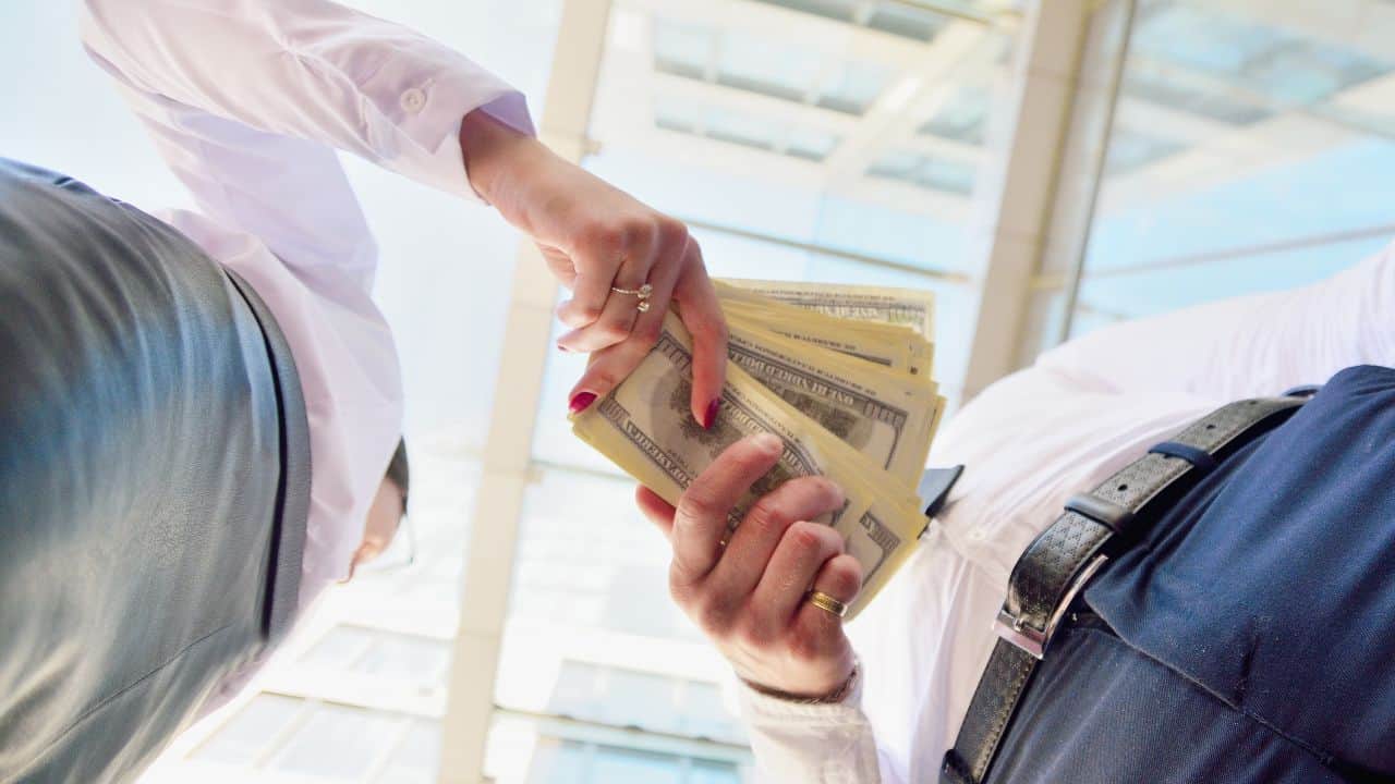 Person handing over a stack of US dollar bills in a professional setting.