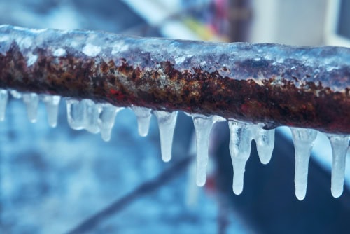 Rusty metal rail covered in ice with icicles hanging down.