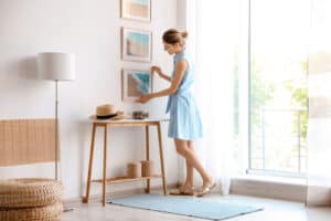 Woman hanging artwork in modern living room with natural light.