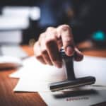 Person stamping approved document on desk for landlord legal compliance.