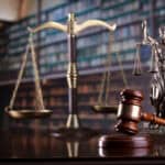 Justice scales, gavel, and Lady Justice statue on a law library desk.