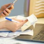 Person reviewing rental documents on a laptop with a smartphone and pen.
