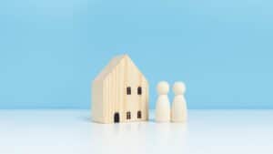 Miniature wooden house with two small figures on a blue background.