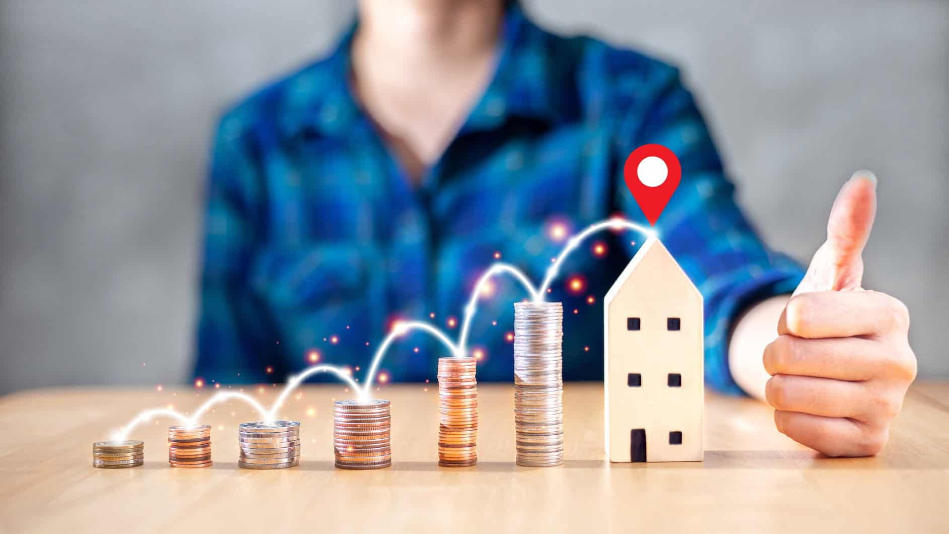 Person showing thumbs up next to stacked coins and house model.