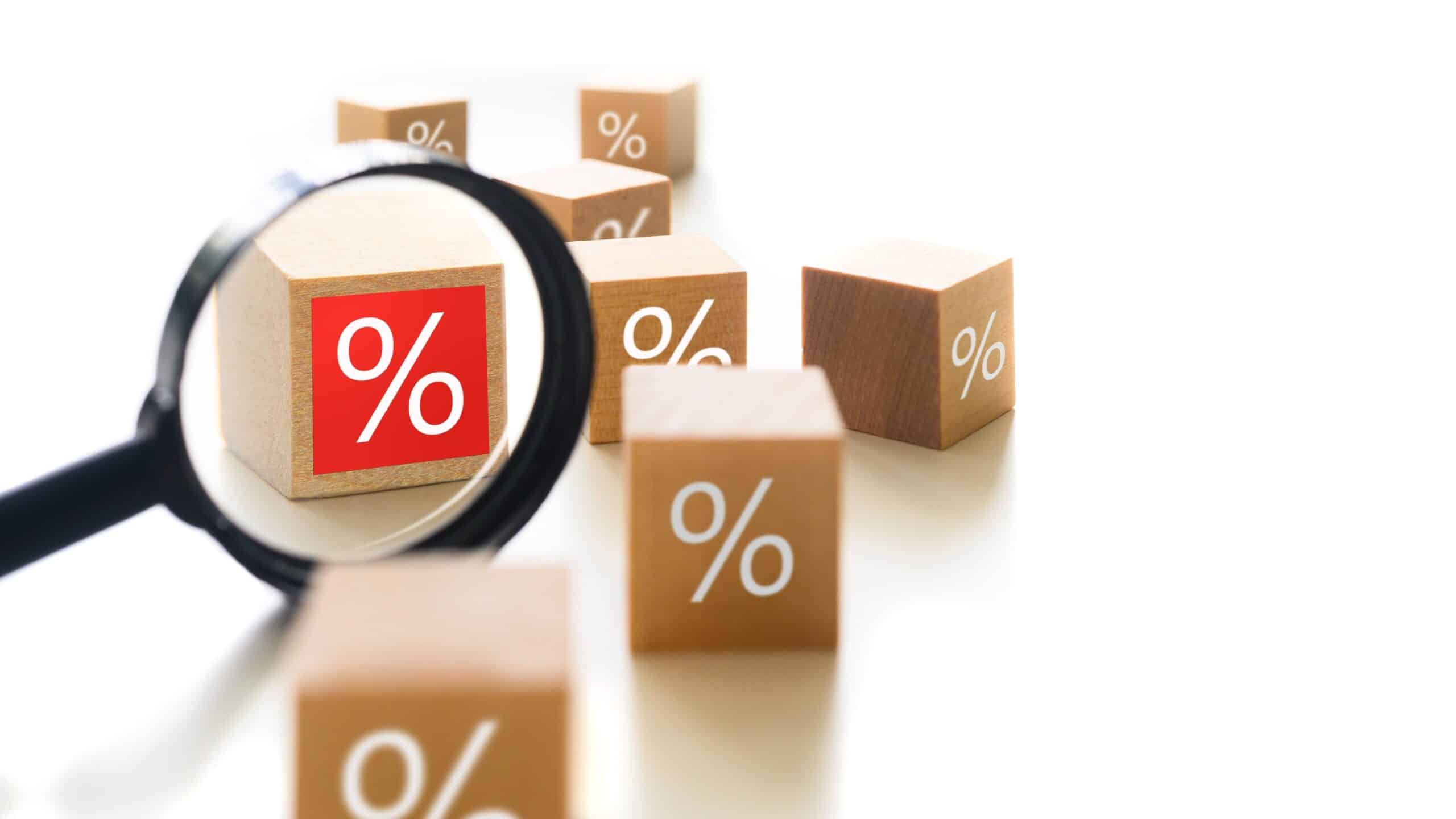 Magnifying glass over wooden blocks with percentage symbols for rental discounts.
