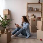 Young woman sitting on the floor with moving boxes in a new home.