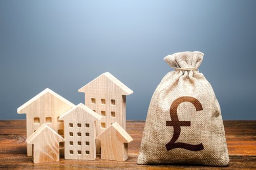 Wooden house models with a money bag and pound sign for property investment.