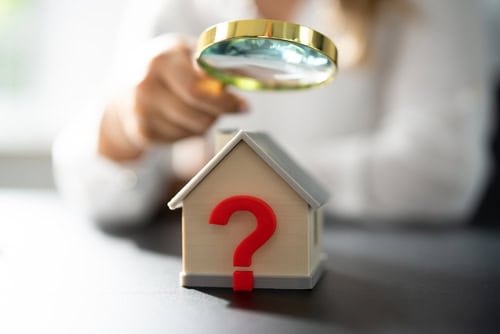 Person inspecting a small house model with a magnifying glass.