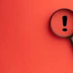 Magnifying glass with exclamation mark on red background.