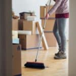 Person sweeping wooden floor in a moving house with boxes around.