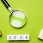 Magnifying glass over 2025 date blocks with small house models.