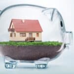 Miniature house inside a transparent piggy bank for property investment.