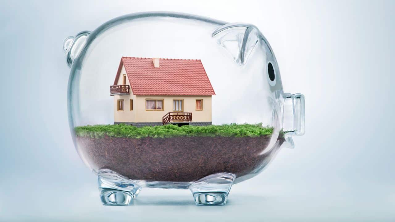 Miniature house inside a transparent piggy bank for property investment.