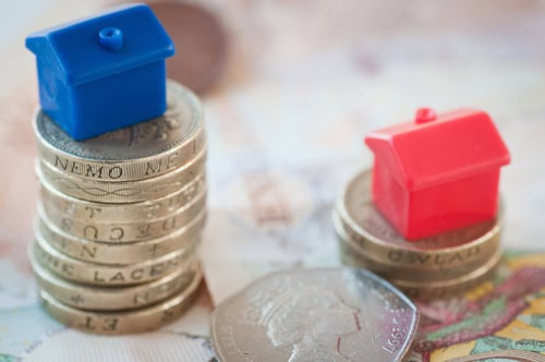 Miniature blue and red houses on stacked coins representing property investment.