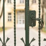 Green metal gate with lock, leading to residential property in a park setting.