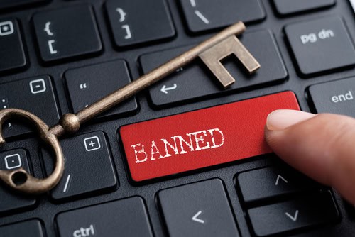 Key with 'BANNED' label on a keyboard with a hand pressing it.